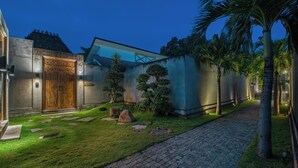 A courtyard with a paved walkway, a wooden door, and a wall with a geometric design.