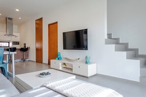 Ein modernes Wohnzimmer mit Flachbildfernseher, weißen Möbeln, einer Treppe und einer Küchenzeile.