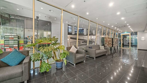 Una hall moderna con parete in vetro, reception e zona relax con piante in vaso.