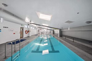 Ein Schwimmbecken mit deutlichen Bahnen, einem Rettungsschwimmerstuhl und einem Hinweisschild für den Ausgang.
