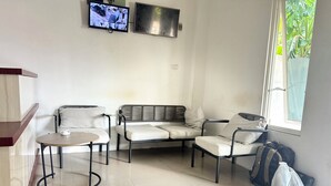 Une pièce comprenant un canapé, deux fauteuils, une petite table, un téléviseur et une fenêtre donnant sur un paysage verdoyant.