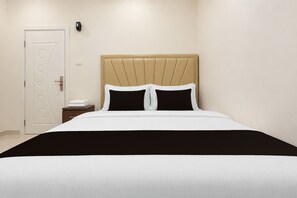 Una habitación de hotel con una cama, una mesita de noche, una puerta y una lámpara fijada a la pared.