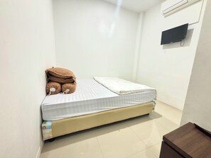 A small, single-bed room with a white mattress and a beige headboard. There is a brown pillow on the bed, and a small brown table is visible in the corner. - Hotel O Medina House (Banda Aceh)