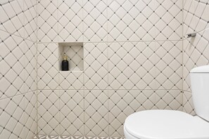 Baño con inodoro, zona de ducha y una botella de champú en un estante pequeño.