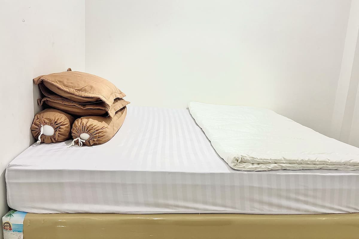 A single bed with a white mattress and a beige pillow.