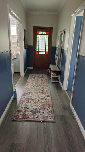 Ein Flur mit Holzboden, einem floralen Teppich, einer Tür mit Buntglasfenster und einem Schuhregal.