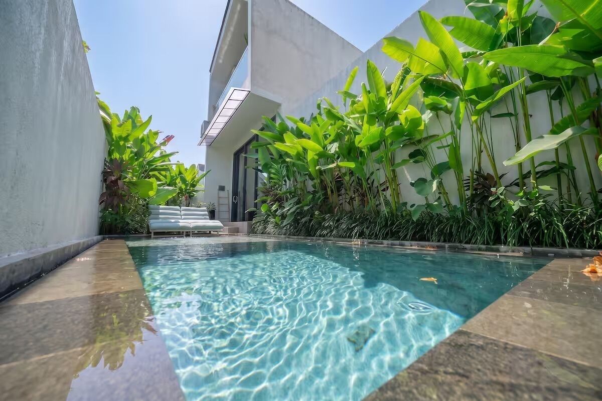 A swimming pool with clear water, surrounded by lush greenery and modern architecture.