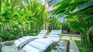 Zona de piscina con sillones de descanso y exuberante vegetación tropical.