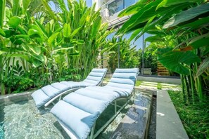 A pool area with lounge chairs and lush tropical plants. - U Villas Pandawa (Badung)