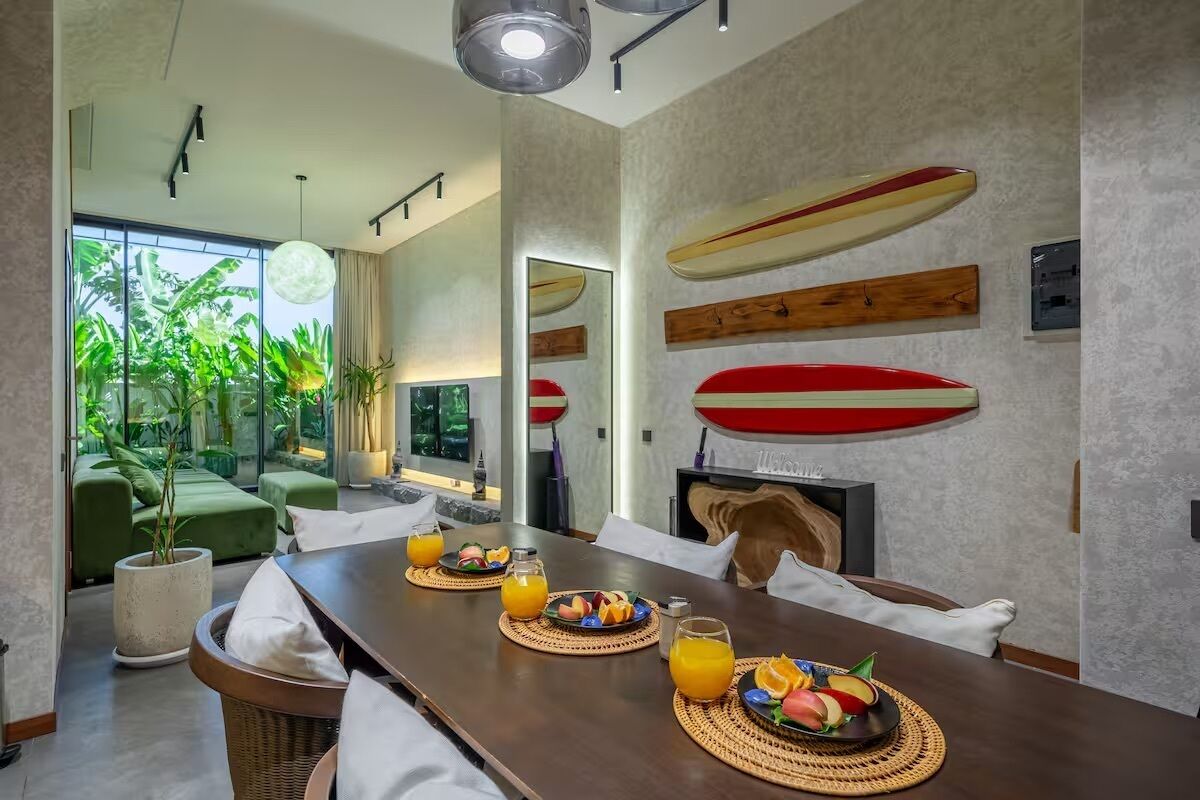 A dining area with a long table, breakfast items, and surfboards on the wall.