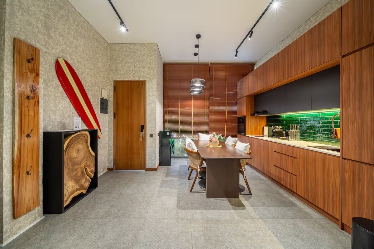 A modern kitchen with wooden cabinets, a dining area with a table and chairs, and a surfboard decoration.