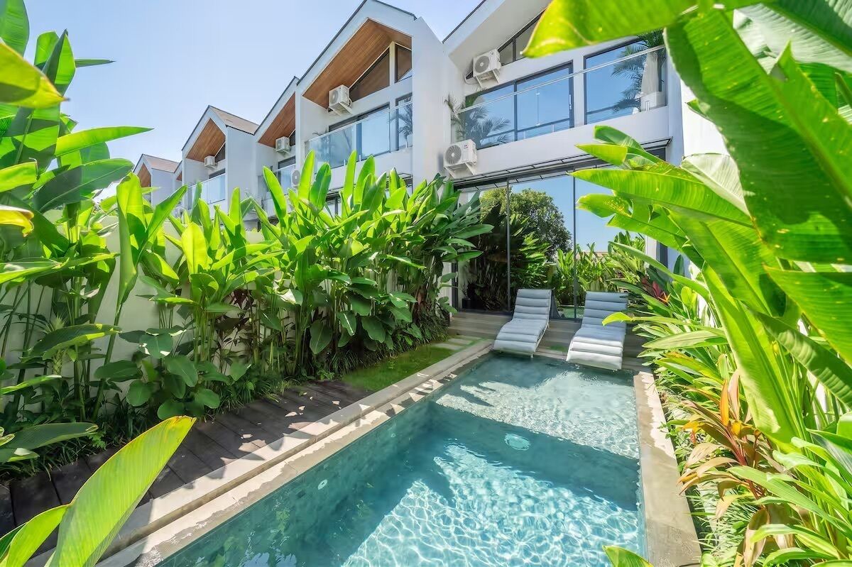 A modern building with a pool surrounded by lush greenery.