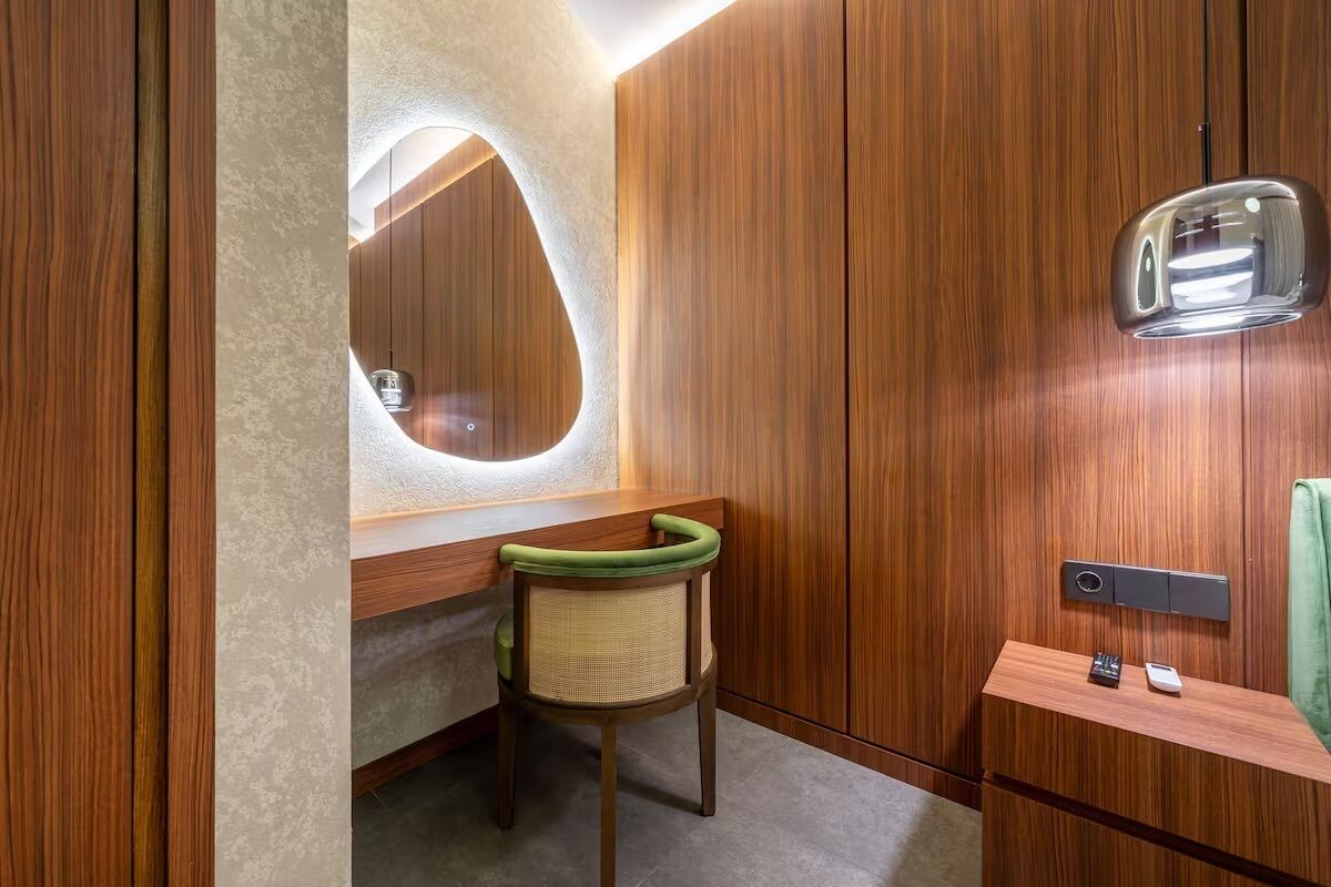 A modern bathroom with a wooden vanity, a green chair, and a mirror with a unique shape.