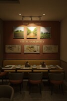 Restaurante com uma mesa comprida, cadeiras e obras de arte penduradas na parede.
