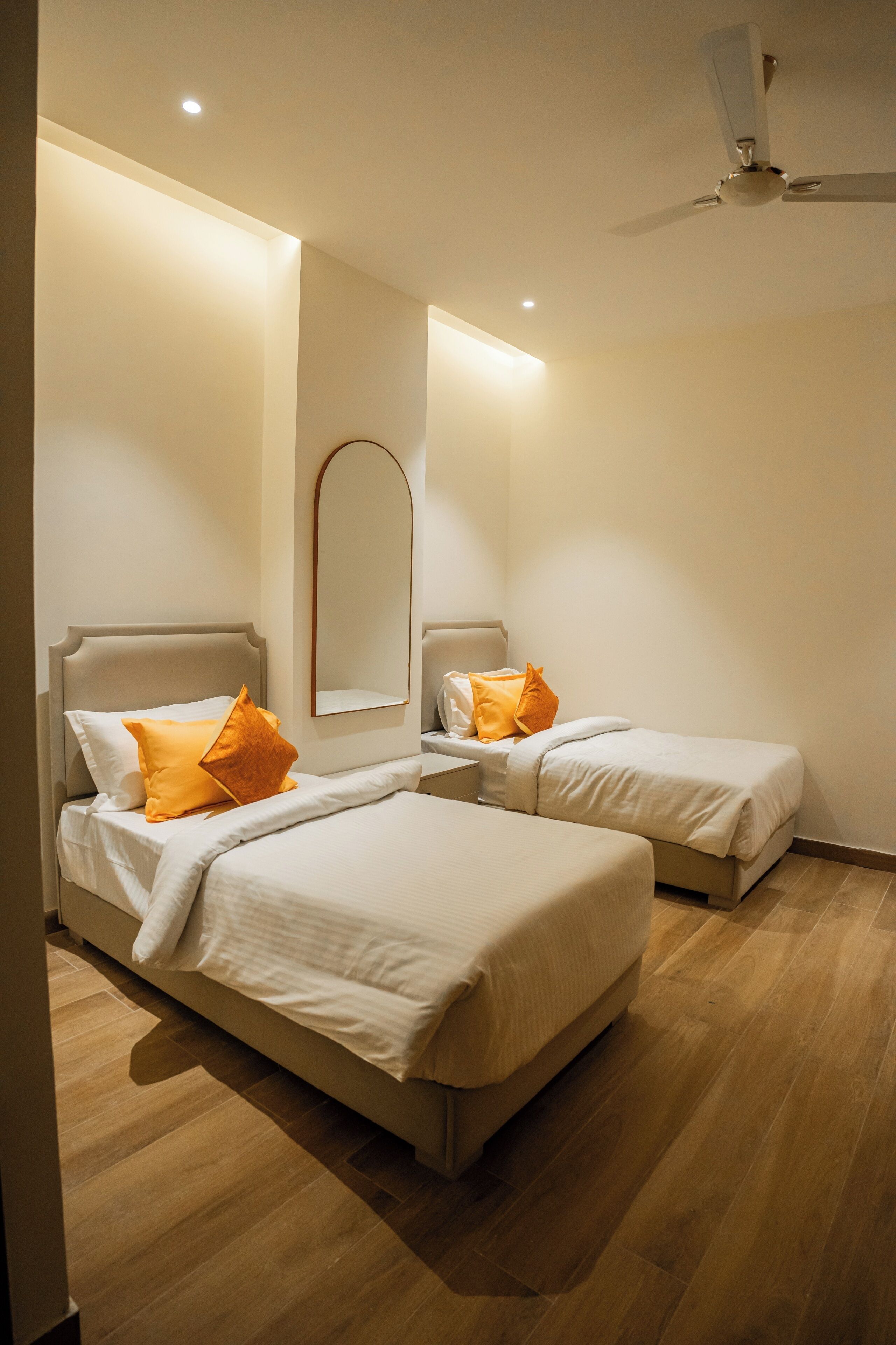 Een hotelkamer met twee bedden, een plafondventilator en een spiegel aan de muur.