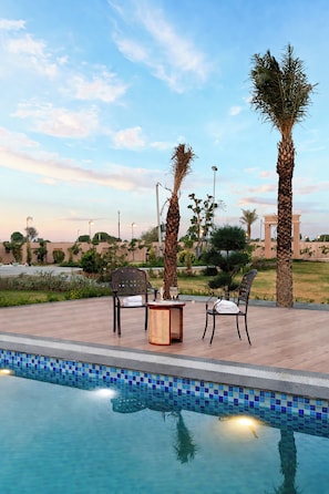 A poolside area with two chairs, a table, and a lamp. - ELIVAAS Nirvana 5BHK Farmhouse with Pool (Amer)