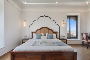 Une chambre à coucher avec un grand lit, une tête de lit en bois, deux tables de chevet, une fenêtre donnant sur un beau paysage et un fauteuil.