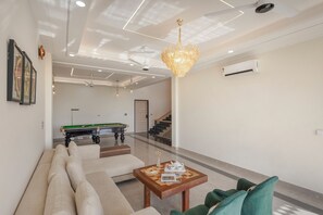 A modern living room with a pool table, green sofas, and a chandelier. - ELIVAAS Nirvana 5BHK Farmhouse with Pool (Amer)
