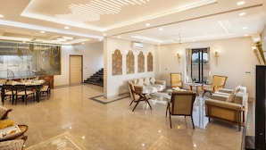A spacious living area with a dining set, sofas, and a TV. - ELIVAAS Nirvana 5BHK Farmhouse with Pool (Amer)