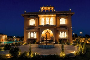 Un edificio tradicional con múltiples ventanas, una entrada central y una fuente en el patio.