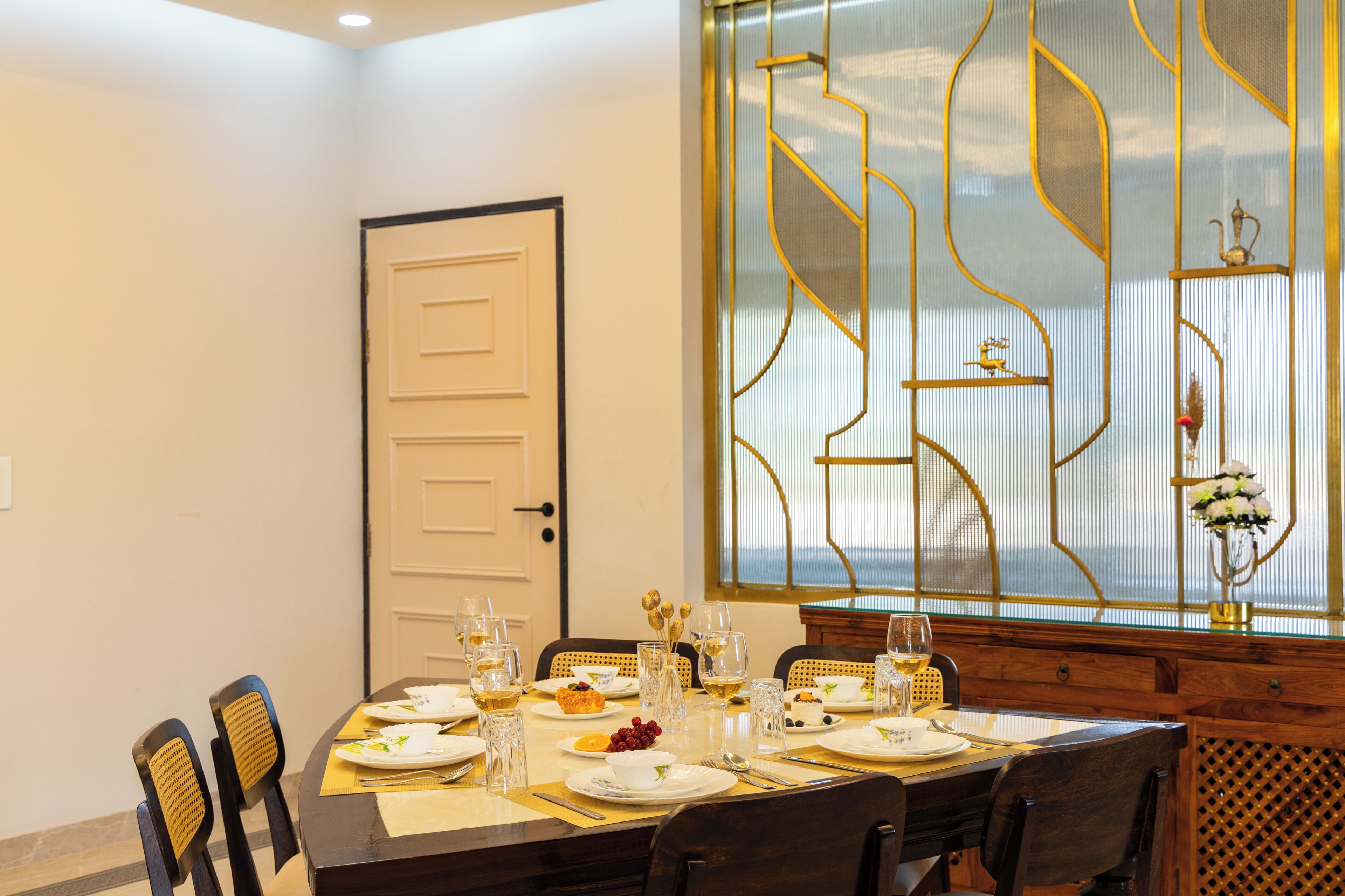 A dining room with a table set for four, chairs, a door, and a decorative window with a view.