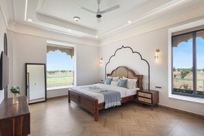 A bedroom with a wooden bed, a nightstand, a wall-mounted TV, and large windows with a view of the outdoors. - ELIVAAS Nirvana 5BHK Farmhouse with Pool (Amer)