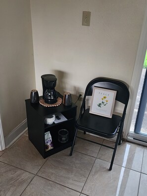 Ein kleiner schwarzer Tisch mit Kaffeemaschine, einem gerahmten Bild und einer Tüte von McDonald's auf gefliestem Boden.