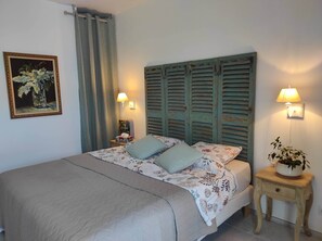 A bed with a quilted bedspread, two pillows, a nightstand with a lamp, a framed picture on the wall, and a potted plant on a side table. - Charming air-conditioned villa in the vineyards, close to the beach (Roquefort-la-Bédoule)