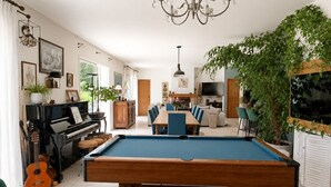 Een ruime woonkamer met een pooltafel, een piano en een eethoek.