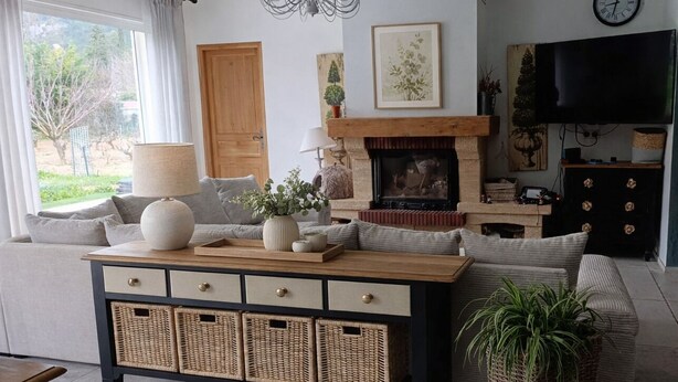Een woonkamer met een bank, een houten salontafel, een open haard, een televisie en een klok aan de muur.