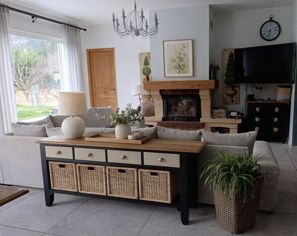 A living room with a sofa, a wooden coffee table, a fireplace, a television, and a clock on the wall. - Charming air-conditioned villa in the vineyards, close to the beach (Roquefort-la-Bédoule)