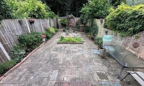 A paved patio with a small garden area, a wooden fence, and a bench.