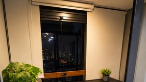 Ein kleiner Balkon mit Tisch und Stühlen, einem Blumentopf und Blick auf eine nächtliche Stadtlandschaft.