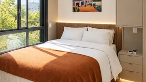 Ein modernes Hotelzimmer mit einem großen Bett, Blick auf Grünflächen, einem Bild an der Wand und einer Deckenleuchte.