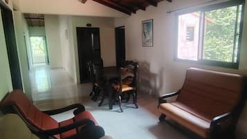 A spacious room with a high wooden ceiling, a dining area with a table and chairs, and a large window with a view of greenery.
