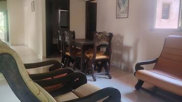 A dining area with a wooden table and chairs, a sofa, and a television in the background.