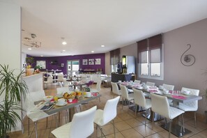 A dining area with white chairs, a long table, and breakfast items. - R Sidence R sid Price St6n (Merville)