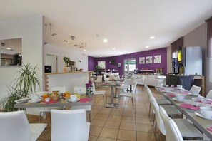 A modern dining area with white chairs, tables set with plates, cups, and a buffet with fruits and pastries. - R Sidence R sid Price St4n (Merville)
