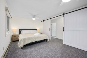 Un dormitorio con cama, mesitas de noche, ventilador de techo y puerta corredera.