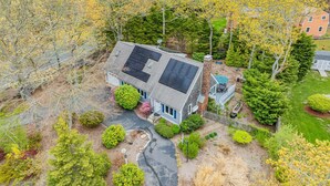 Uma casa com painéis solares, cercada por árvores e um gramado bem cuidado.