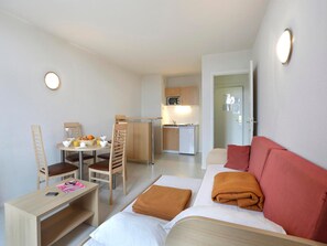 A compact hotel room with a kitchenette, a dining area, and a bed with a red accent pillow. - Les Demeures Champenoises 2p4s (Epernay)