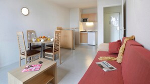Un espacio habitable compacto con comedor, kitchenette y un sofá con una revista.