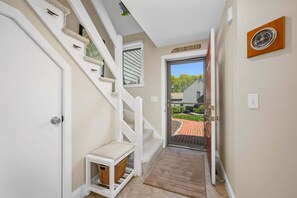A hallway with a white staircase, a door labeled 'NEW SEABURY,' and a small bench with a basket. - Sea Spark - Cape Escape with Pool Access (Mashpee)