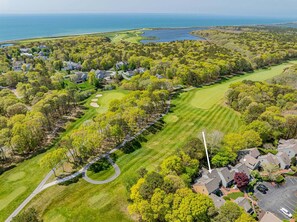An aerial view of a residential area with houses, a golf course, and a body of water. - Sea Spark - Cape Escape with Pool Access (Mashpee)