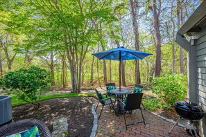 A patio with a table and chairs, a grill, and a blue umbrella. - Sea Spark - Cape Escape with Pool Access (Mashpee)