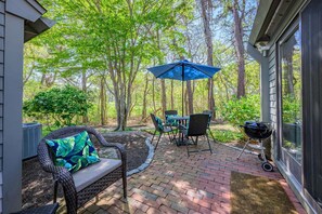 A patio with a table and chairs, a grill, and a blue umbrella. - Sea Spark - Cape Escape with Pool Access (Mashpee)