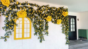 Eine Wand mit gelben Rosen, ein Fenster, eine schwarze Tür und eine grüne Bank.