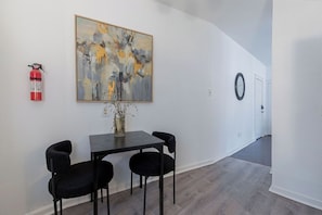 Ein Flur mit Essbereich, der einen Tisch, Stühle, einen Feuerlöscher und ein Bild an der Wand zeigt.