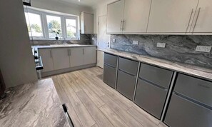 A modern kitchen with light wood flooring, grey cabinets, and a marble backsplash. - Room-small Double in Quiet House - Chelm (Chelmsford)