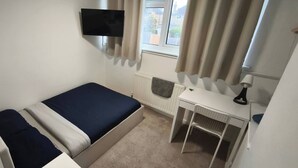 A small, single-bed room with a desk, a chair, a TV mounted on the wall, and a window with curtains. - Room-small Double in Quiet House - Chelm (Chelmsford)